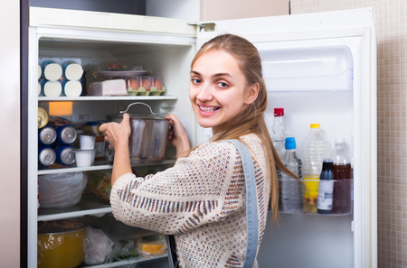 Smiling young blonde housewife arranging products on fridge shelvesの写真素材