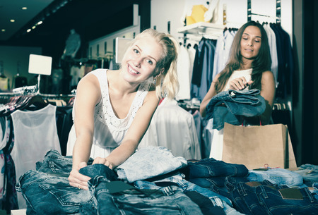 Two laughing girls choosing denim trousers together in clothes storeの写真素材