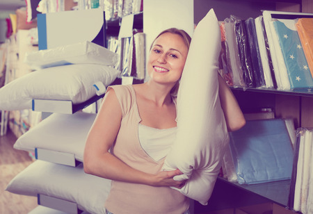 portrait of smiling  female customer choosing pillow in bedding section in shopの写真素材