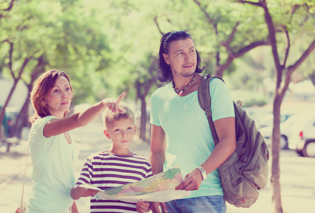 Happy family of three searching way at paper map in the city parkの写真素材