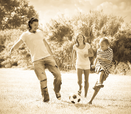 Middle-aged couple and teenager son playing with soccer ball  at summer parkの写真素材