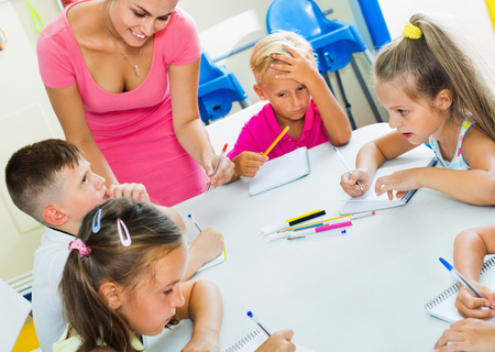 Happy smiling diligent kids writing together with tutor at school class indoorsの写真素材