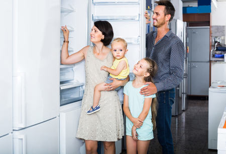 smiling spanish family of four shopping new refrigerator in home appliance storeの写真素材