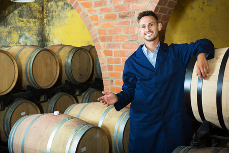 portrait of young smiling male wine maker in coat working in winery cellarの写真素材