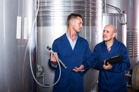 cheerful two experts men standing with clipboard in wine processing sectionの写真素材
