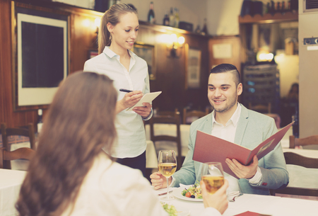 Handsome man with beautiful happy girlfriend making order in cafeの写真素材