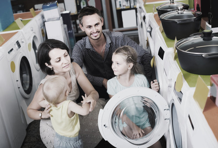 cheerful russian parents with two kids choosing washing machine in home appliance storeの写真素材