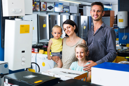 smiling parents with two kids standing in home appliance storeの写真素材