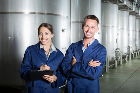 Two young winery employees standing in protective uniform and taking notes in secondary fermentation sectionの写真素材