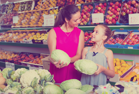 portrait of young woman with girl buying cabbage on marketplaceの写真素材