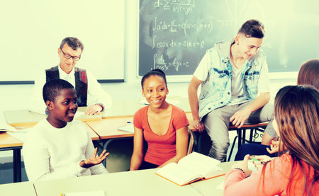 Friendly students of different nationalities sitting and talking in the classroom while the break