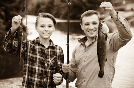 Happy teenage boy and his father holding fish on hook in handsの写真素材