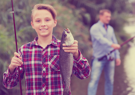 Portrait of laughing teenager boy having fish in hands outdoorsの写真素材
