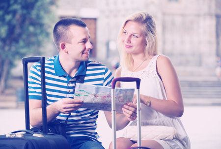 Young cheerful traveling couple searching for direction using paper map in townの写真素材