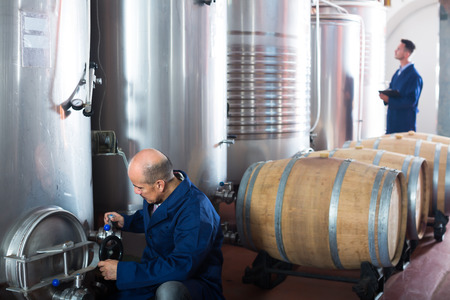 Glad man machinery operator working on secondary fermentation equipment in winery manufactoryの写真素材