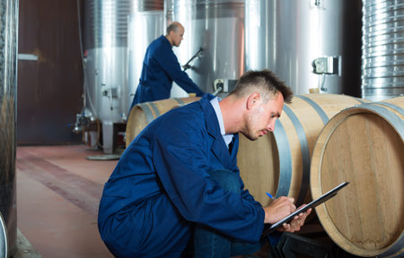 young man working in secondary fermenting section on winery and taking notes
