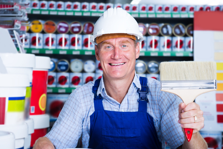 Glad workman in hardhat buying painting roller in household storeの写真素材