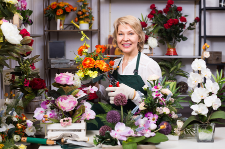 Portrait of smiling mature woman florist with clippers making flowers ready for saleの写真素材