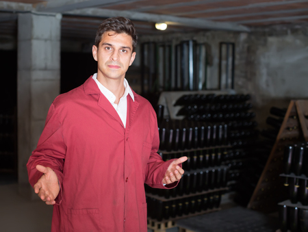 friendly man wearing uniform working with bottle storage racks in winery cellarの写真素材