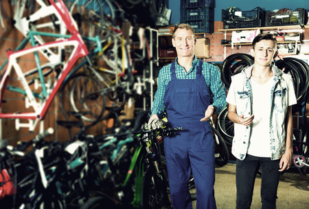 Man seller helping teenager boy to buy right bike in sport shopの写真素材