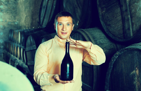happy man holding bottle of wine in winery cellar