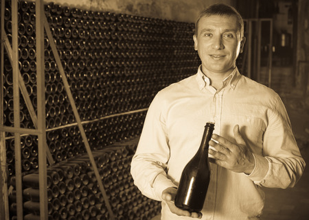 Satisfied customer holding bottle of red wine from dusty shelvesの写真素材