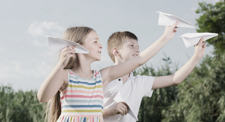 two positive kids playing with simple paper planes on sunny dayの写真素材