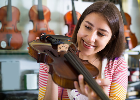 Happy longhaired girl choosing full size violin in music shop and smilingの写真素材
