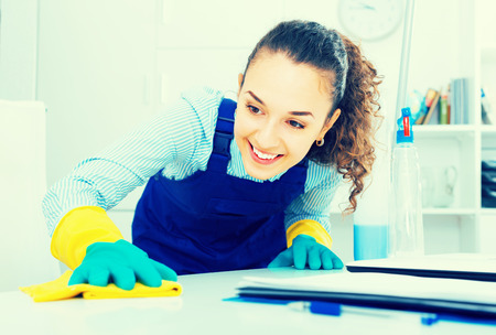 joyful female professional cleaner in working overall  dusting in modern officeの写真素材