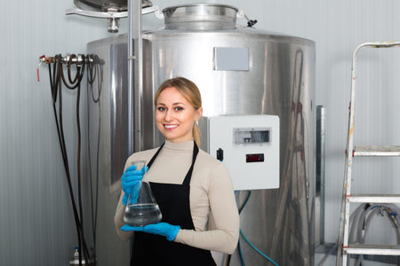 Portrait of joyful young female worker near tank on beer brewery factory