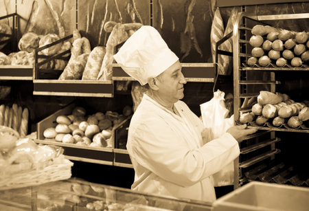 Portrait of positive baker with fresh bread smiling in bakery