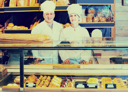 smiling russian  staff offering fresh baguettes and buns in bakery
