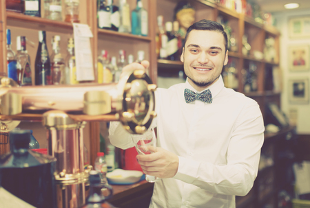 Modern bar with bottles at background and happy smiling male bartenderの写真素材