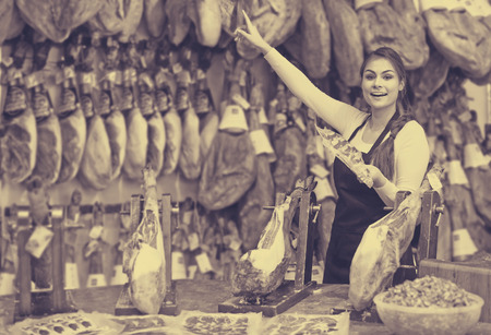 happy european female butcher with lard and meat in counter of storeの写真素材