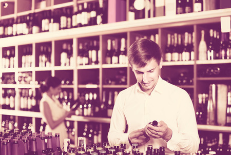 portrait of happy russian  glad male customer taking bottle of wine in storeの写真素材