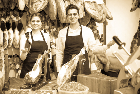 Successful adult sellers offering tasty jamon for customers in shopの写真素材