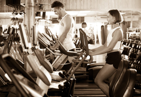 Young smiling woman warming up using elliptical machine in gym indoors