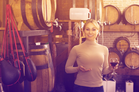 Smiling young woman tasting wine from wood in wine houseの写真素材