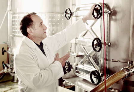 Elderly  positive man in uniform works with equipment to winery
