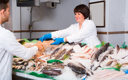 friendly woman selling fish to male customer in storeの写真素材