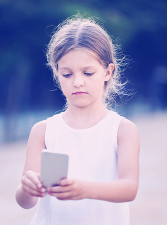 Portrait of serious girl  in elementary school age looking at mobile phone outdoorsの写真素材