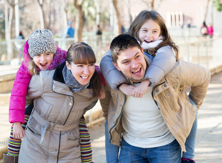 Portrait of happy young parents playing with little daughters at slide of playground. Focus on parentsの写真素材