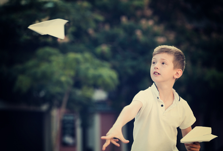 smiling boy in elementary school age playing with flying paper planes outdoorsの写真素材