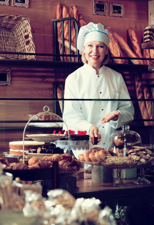 Pretty senior woman selling fresh pastry and baguettes in local bakeryの写真素材