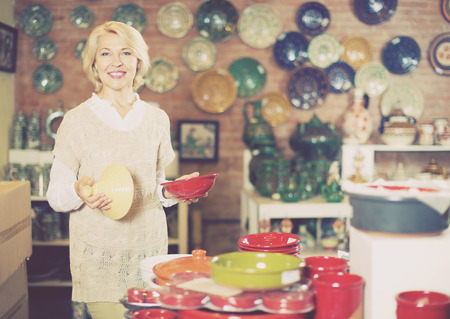 Smiling mature female holding  ceramic cookware at supermarketの写真素材