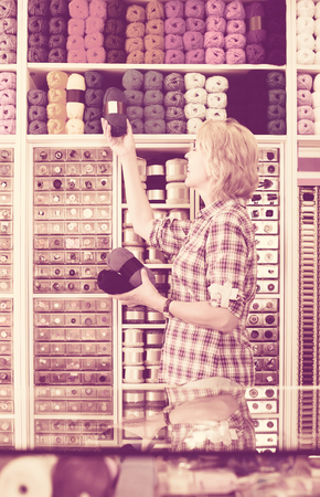 portrait of mature happy american  female cashier standing at cash desk in embroidery shopの写真素材