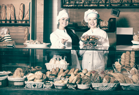 Two positive women selling bread and different pastry in bakeryの写真素材