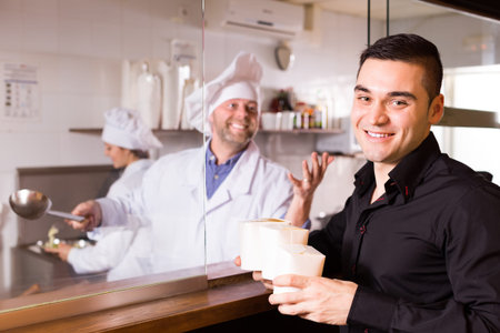 Cheerful smiling man purchasing fast food in cardboard box at cafe