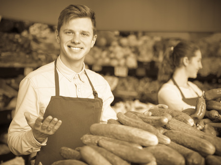 happy american  stuff in apron selling green cucumber at marketplaceの写真素材