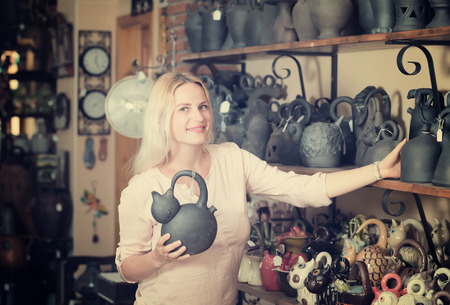 Portrait of cheerful woman choosing black glazed ceramic utensil in boutiqueの写真素材